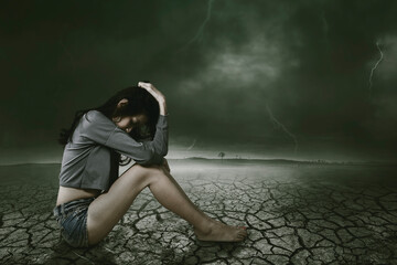 Sad alone woman in the cracked land and thunderous sky