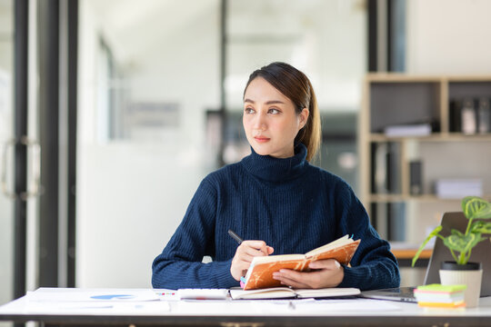 Smiling Asian Woman Working On Laptop At Workplace, Dreaming Of Something With Happy Face Looking Away From Camera, Thinking While Sitting Near Computer