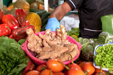 unrecognizable man's hand holding plate full of ginger next to tomato and paprika at market stall