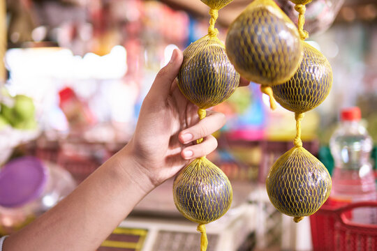 unrecognizable man's hand in close-up holding borojo hanging on netting in marketplace