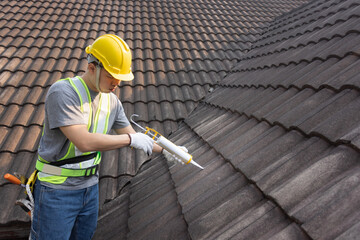 Worker man using silicone sealant adhesive  to fix crack of the old tile roof. - 576174309