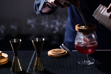 Bartenders making the cocktail glass on the bar counter in the dark background.