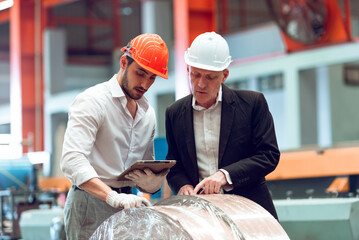 Factory worker engineer wearing protective helmets using tablet for inspect machine system in factory. Heavy metal industry manufacturing factory.
