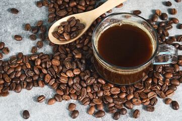 Mug of invigorating black coffee coffee and beans in spoon full on gray background, closeup