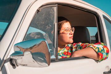portrait of young adult woman looking at the landscape from a classic car at sunset