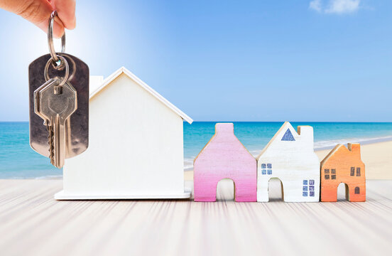 House key with miniature house over beach background, summer holiday accommodation, property and real estate business concept, holiday house