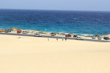 Obraz premium A spectacular paved road that passes through the desert and sand dunes of Corralejo in Fuerteventura. Contrast between ocean and desert territory.