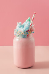 A glass jar with a strawberry milkshake topped with cotton candy