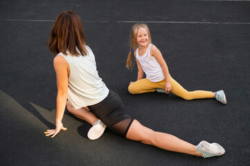 Mother and daughter go in for sports outdoors. Caucasian woman and little girl are engaged in fitness at the stadium.