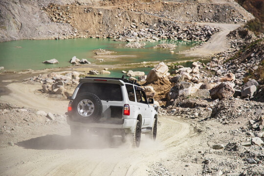 White off-road suv car descends to the mountain lake surrounded by rocky terrain.