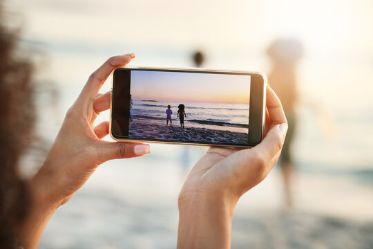 Phone, photograph and beach with a woman in nature, recording her playing kids by the ocean outdoor. Mobile, family and sunset with a parent taking a picture of her kids on the sand at the sea