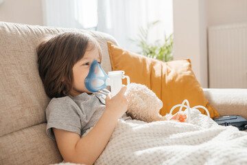 Little boy makes inhalation with a nebulizer at home lying on the couch. Cough prevention and...