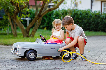 Two happy children playing with big old toy car in summer garden, outdoors. Kid boy refuel car with...