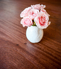 mini bouquet of pink roses in a white handmade vase on a dark wooden background