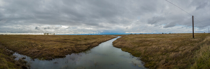 Panorama of a creek meandering through a grass field in winter 