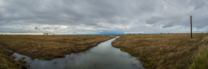Fototapeta na wymiar Panorama of a creek meandering through a grass field in winter 