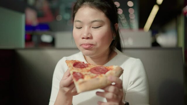 pizza lover asian woman Enjoying Pizza Holding And Biting Tasty Slice Sitting At Table while waiting for her trian at train station,Young happiness asia female have a pizza lunch break.