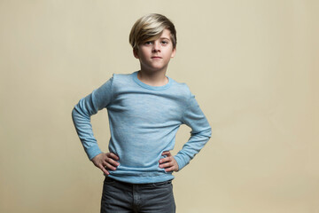 Obraz premium A serious boy of 9-10 years old stands near a yellow wall. A guy in a blue sweater and gray jeans keeps his hands on his belt. Confidence and positivity.