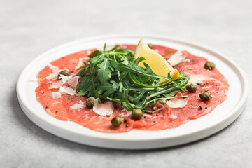 Beef carpaccio with capers, arugula and parmesan on a gray concrete background, selective focus