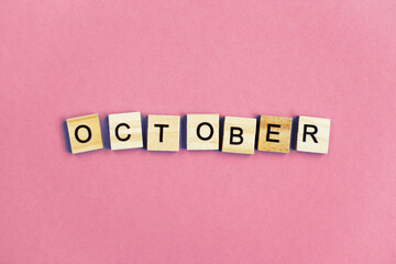 inscription October made by wooden cubes on a pastel pink background.