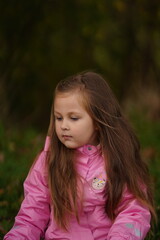 Little girl in a red coat catches autumn leaves sitting on a blanket on the foliage in a park in nature in fall. A child in warm clothes is having fun and playing in the forest