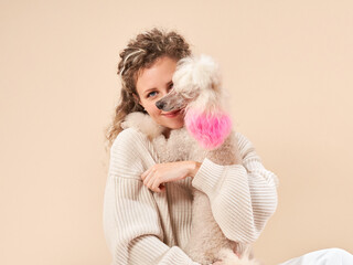 Cute girl with a dog on a beige background. Curly woman with white poodle. cozy with a pet