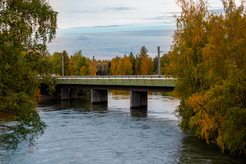 Fototapeta na wymiar View of the bridge over the flowing river. Power lines over the bridge. Birch trees, autumn foliage.
