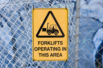 A yellow sign with black text warning of forklifts operating in this area - obrazy, fototapety, plakaty