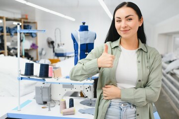 Fototapeta premium Young woman working as seamstress in clothing factory.