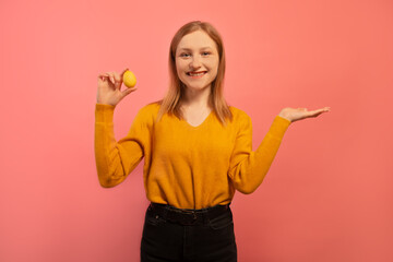 Happy smiling young woman shows yellow painted dyed easter egg and holds palm up hand  to insert an ad, text words isolated on pink background. Copy space, place for advertisement.

Easter concept.