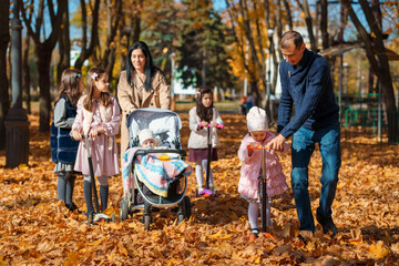 big family spends time together in autumn city park, children and parents, happy people walk and relax, ride scooters, beautiful nature, bright sunny day and yellow leaves