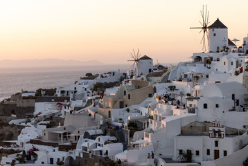 Fototapeta na wymiar Whitewashed houses and windmills in Oia in warm rays of sunset on Santorini island. Greece