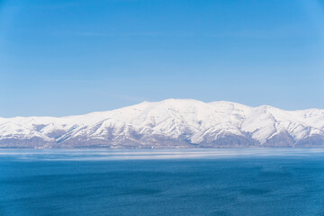 Aerial panorama view snow covered mountains. Snowy mountain ridge on winter sunrise. Stunning mountains range covered with snow over beautiful lake