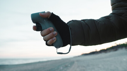 Man pilot a drone with remote single hand controller on the beach near the ocean