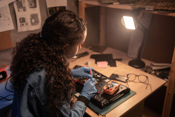 Fototapeta na wymiar Computer retro repair shop. Female engineer performing laptop maintenance. Hardware developer fixing electronic components, voltage measurement with multimeter