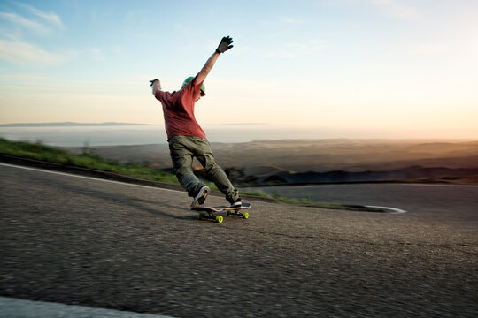 Downhill skating athlete slides around a turn on a windy mountain road above Santa Barbara, California as the sun sets.