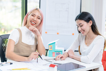 Fototapeta premium Concept of engineering consulting, Two female engineers discussing about model of building together; Two female architects are studying blueprint of building house.