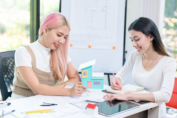 Concept of engineering consulting, Two female engineers discussing about model of building together; Two female architects are studying blueprint of building house.