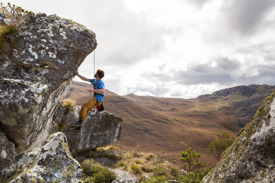 A Male Climber Looks At A Climb And Tests The Quality Of The Rock While Hanging From A Rope