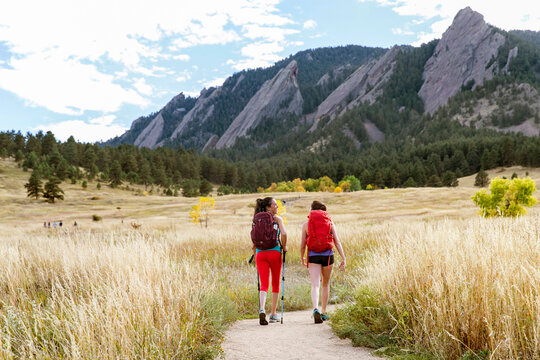 female hikers walk on a trail beneath the flatirons in Colorado