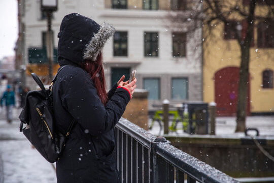 Woman taking picture with smartphone on bridge in winter, Copenhagen, Denmark