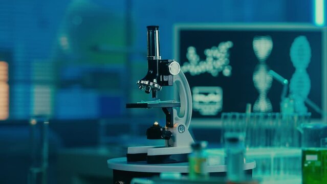 Microscope, glass test tubes and flasks on the background of a computer monitor depicting the structure of DNA. Modern medical research laboratory or hospital. Empty workplace in blue light. Close up.