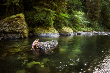 CASCADE LOCKS, OREGON, USA. A woman in biking climbs onto a rock in the middle of a clear river pool of the Columbia River Gorge.