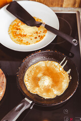 Making thin pancakes on frying pan in kitchen, with cooking dough for crepes and pancakes