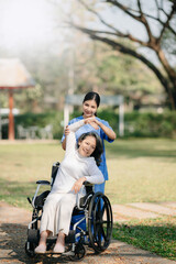 Asian careful caregiver or nurse and the happy patient in a wheelchair are walking in the garden to help and encourage and rest your mind with green nature. 