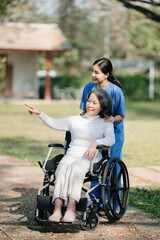 Elderly asian senior woman on wheelchair with Asian careful caregiver and encourage patient, walking in garden. with care from a caregiver and senior health insurance...
