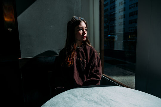 Calm teen girl sitting in cafe looking out of window