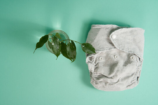 Washable Ecological Fabric Cotton Diapers On A Light Green Background. A Twig Of A Tree With Leaves Next To It As A Concept Of Renewable Green Energy. Natural Resources.