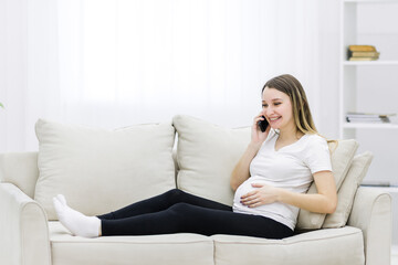 Pregnant woman talking over the phone on white sofa.