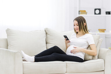 Obraz premium Young pregnant woman on white sofa using phone.
